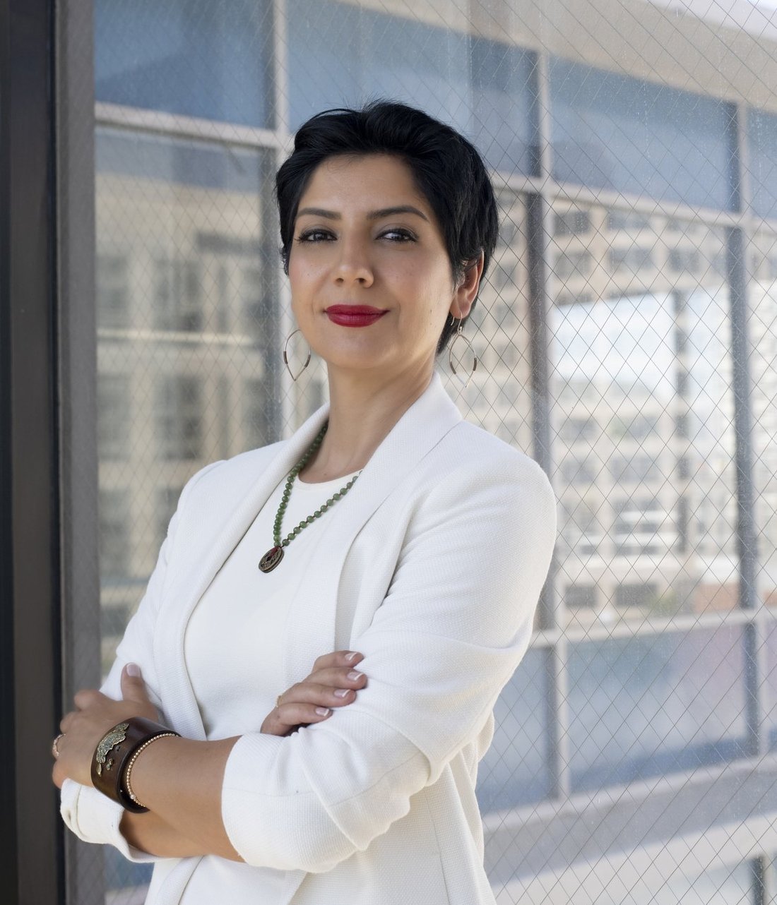 Anush Gagua in a white suit, arms crossed, in front of a city window